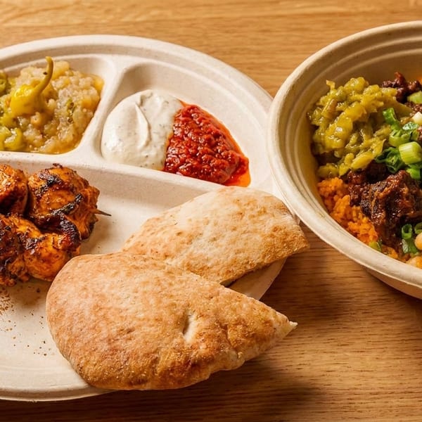 Grilled chicken skewers, pita bread, sauces, and a bowl of rice, chickpeas, and meat.
