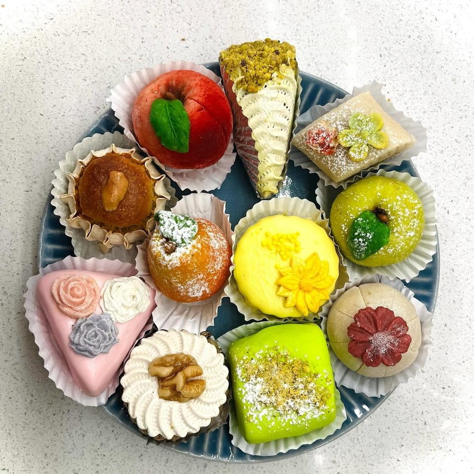 A blue plate holds a variety of colorful, intricately decorated pastries and desserts in white paper cups.